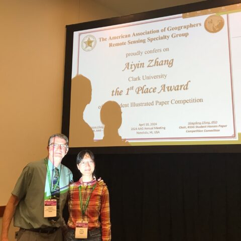 Dr. Robert Gilmore Pontius and Aiyin Zhang posing in front of a screen displaying an award certificate.